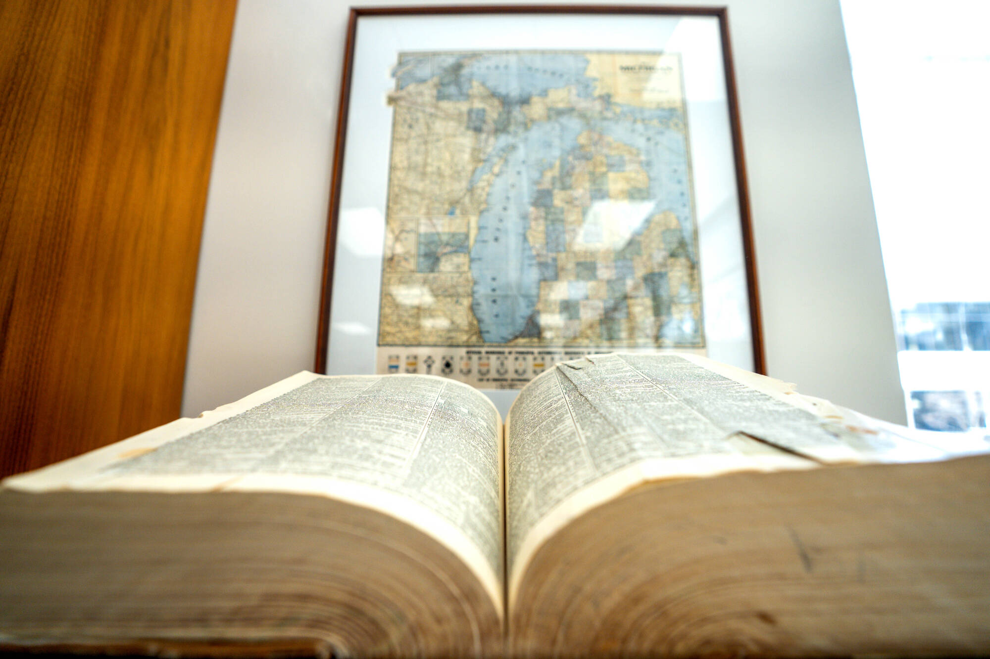 book open on desk in front of a framed map of Michigan